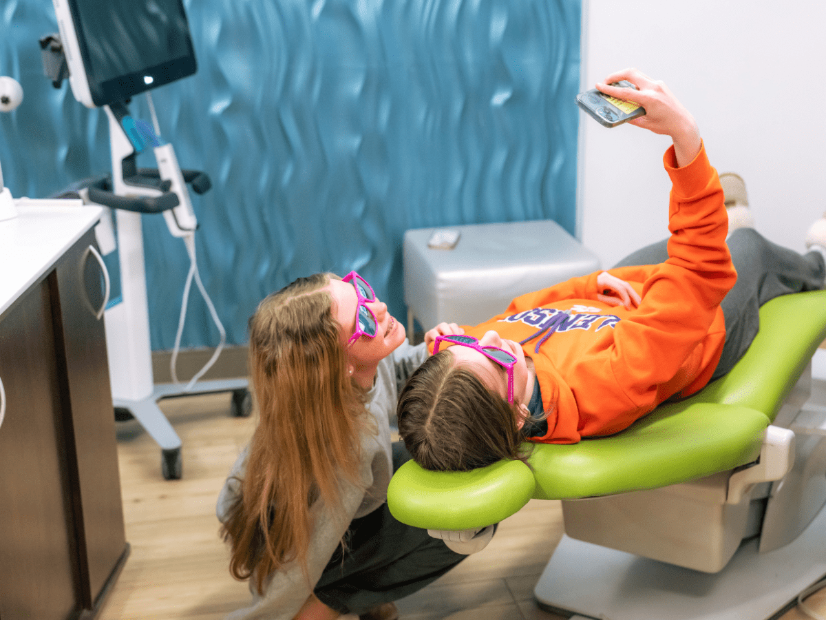 Teen patient in the treatment chair taking a selfie while wearing sunglasses at Spark Orthodontics