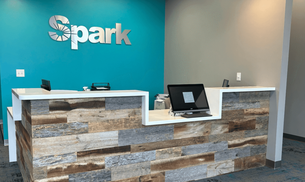 Reception desk with a large Spark logo on a teal wall at the Spark Orthodontics Hazleton, PA office