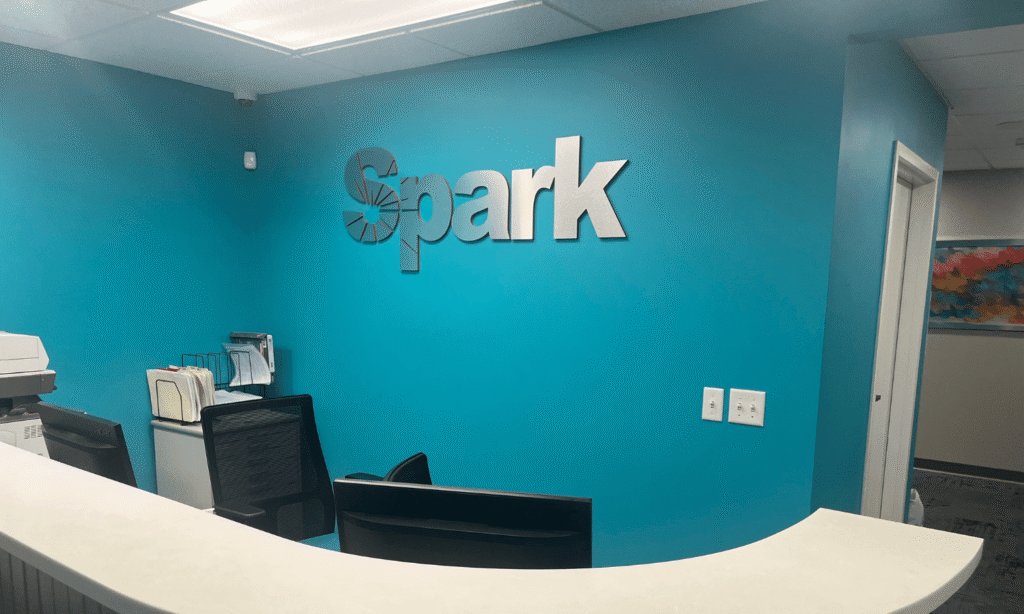 Reception desk with a teal Spark logo wall at the Spark Orthodontics Lancaster, PA office