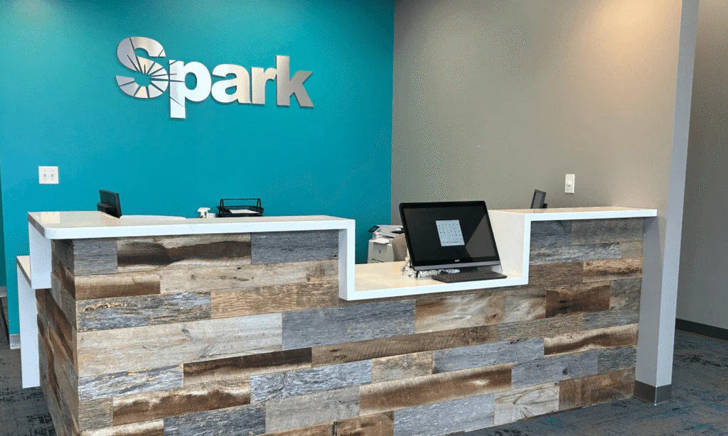 Reception desk with a large Spark logo on a teal wall at the Spark Orthodontics Hazleton, PA office